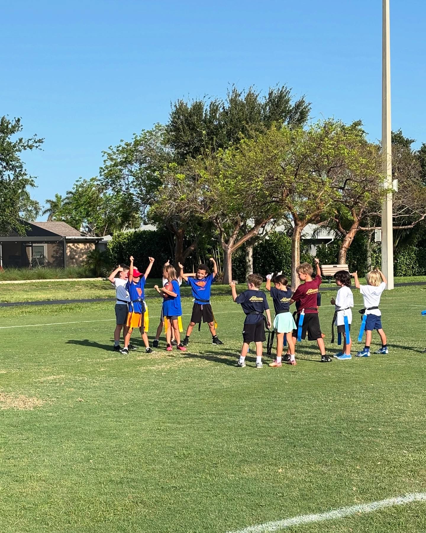 OCMI kids playing flag football in a Marco Island park wearing DERO Roofing shirts during community event